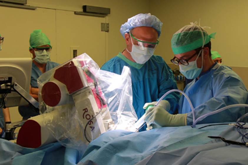 Above is a photo of a medical resident and faculty member working in a small surgical field, with another member of the medical team watching nearby.